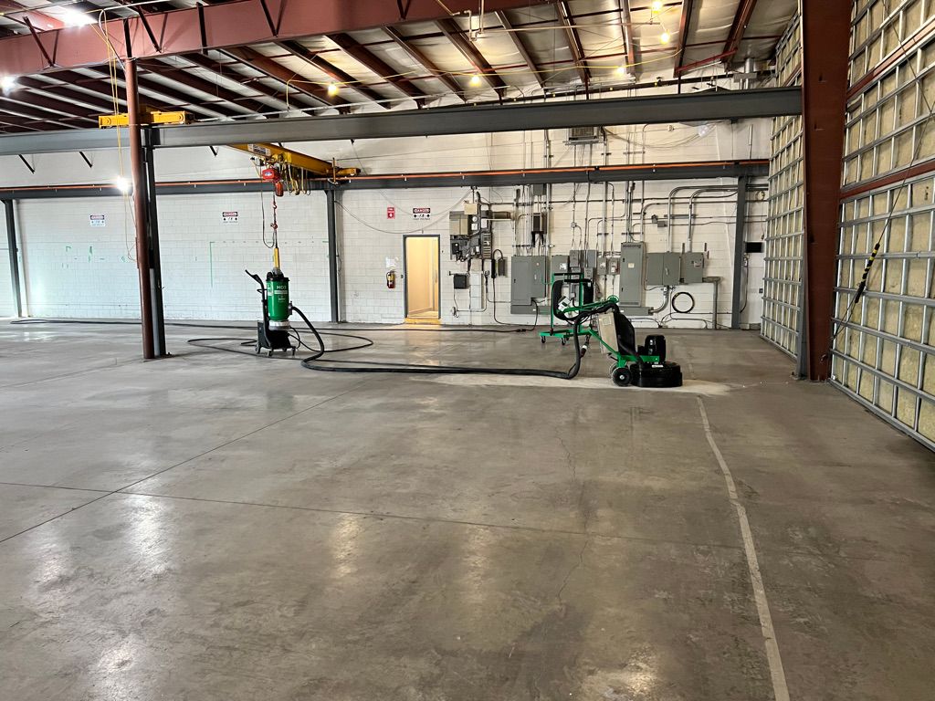 Large industrial high-tech warehouse with concrete floor, two green floor grinding machines, yellow overhead crane and electrical panels