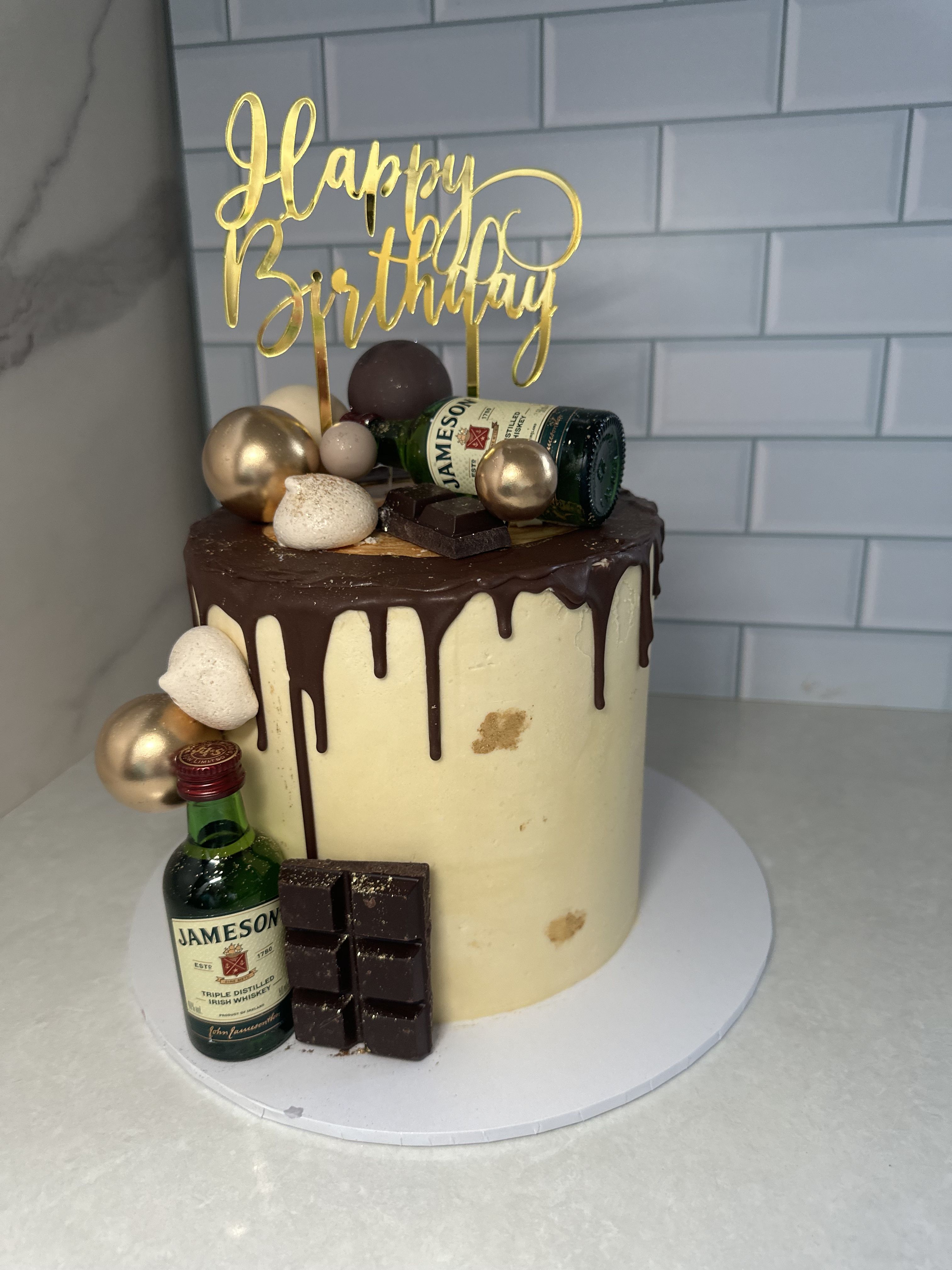 Chocolate drip cake with mini Jameson bottles and gold happy birthday topper