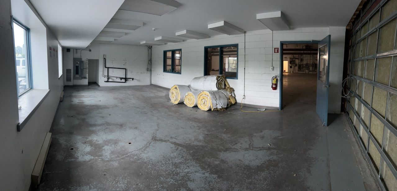 Empty industrial room with concrete floor, white walls, insulation rolls, blue door and fire extinguisher — pre-installation state