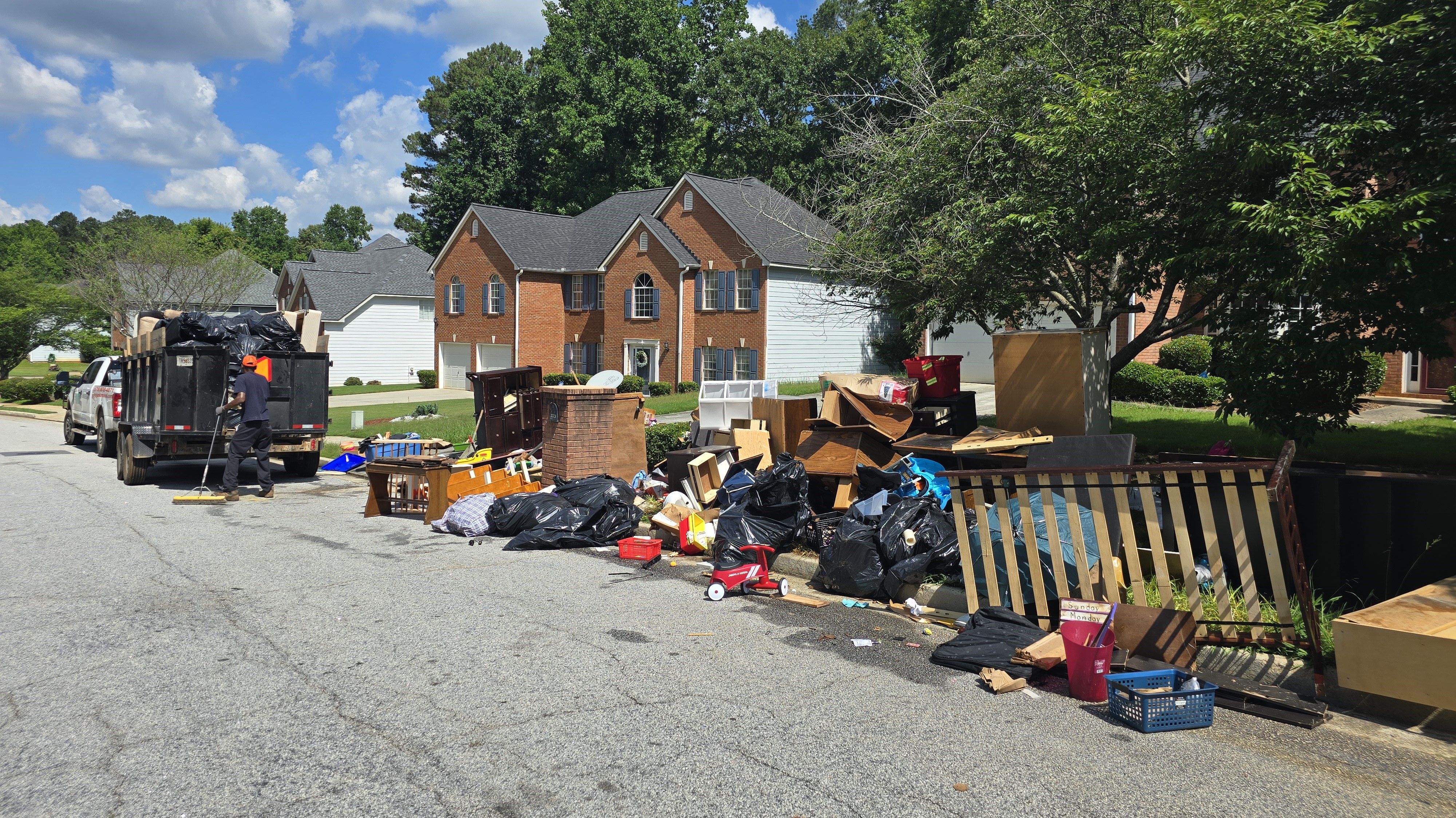 Curbside cleanout in progress - GoGo Junk Removal technician sweeping and staging curb pile next to white truck