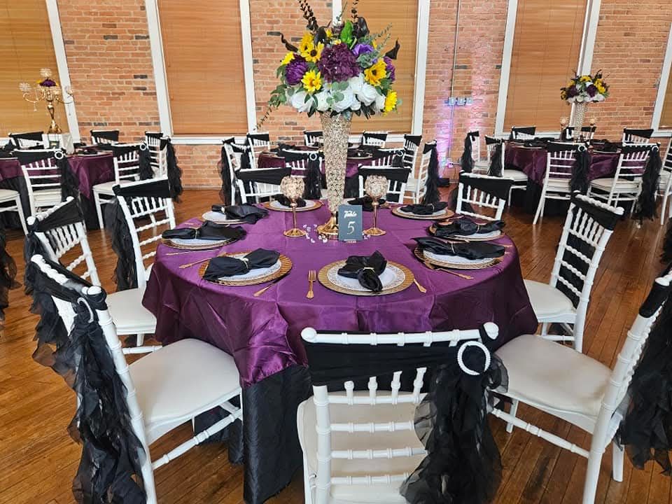 Elegant banquet setup with purple tablecloths, sunflower centerpieces, and gold place settings