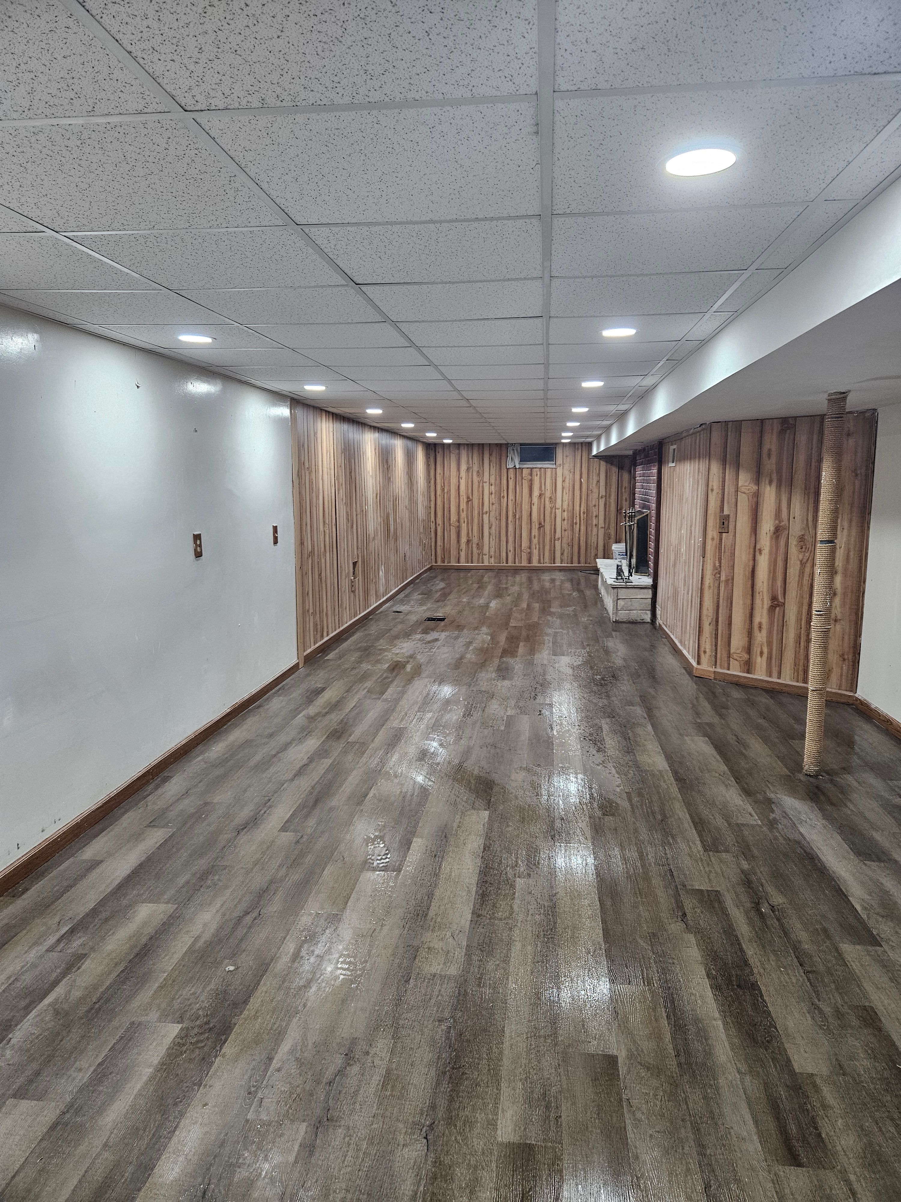 Finished basement with wood paneling and fireplace surround