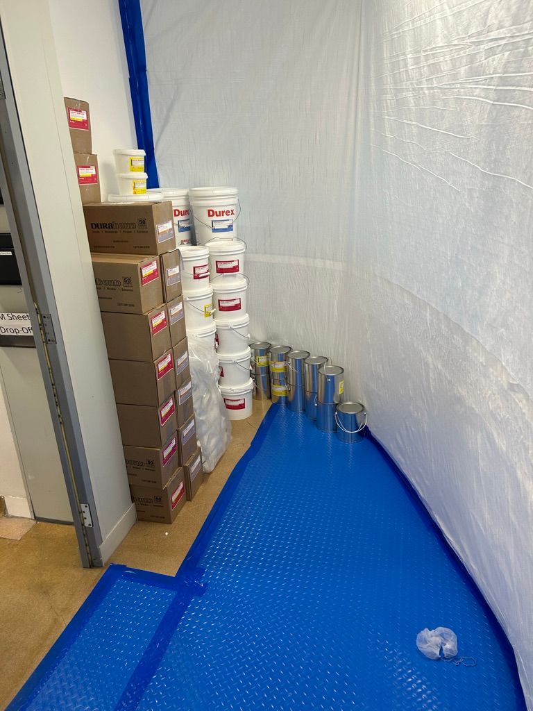 Pharmaceutical installation materials staged on blue protective floor covering — Durabond product buckets and paint cans ready for application