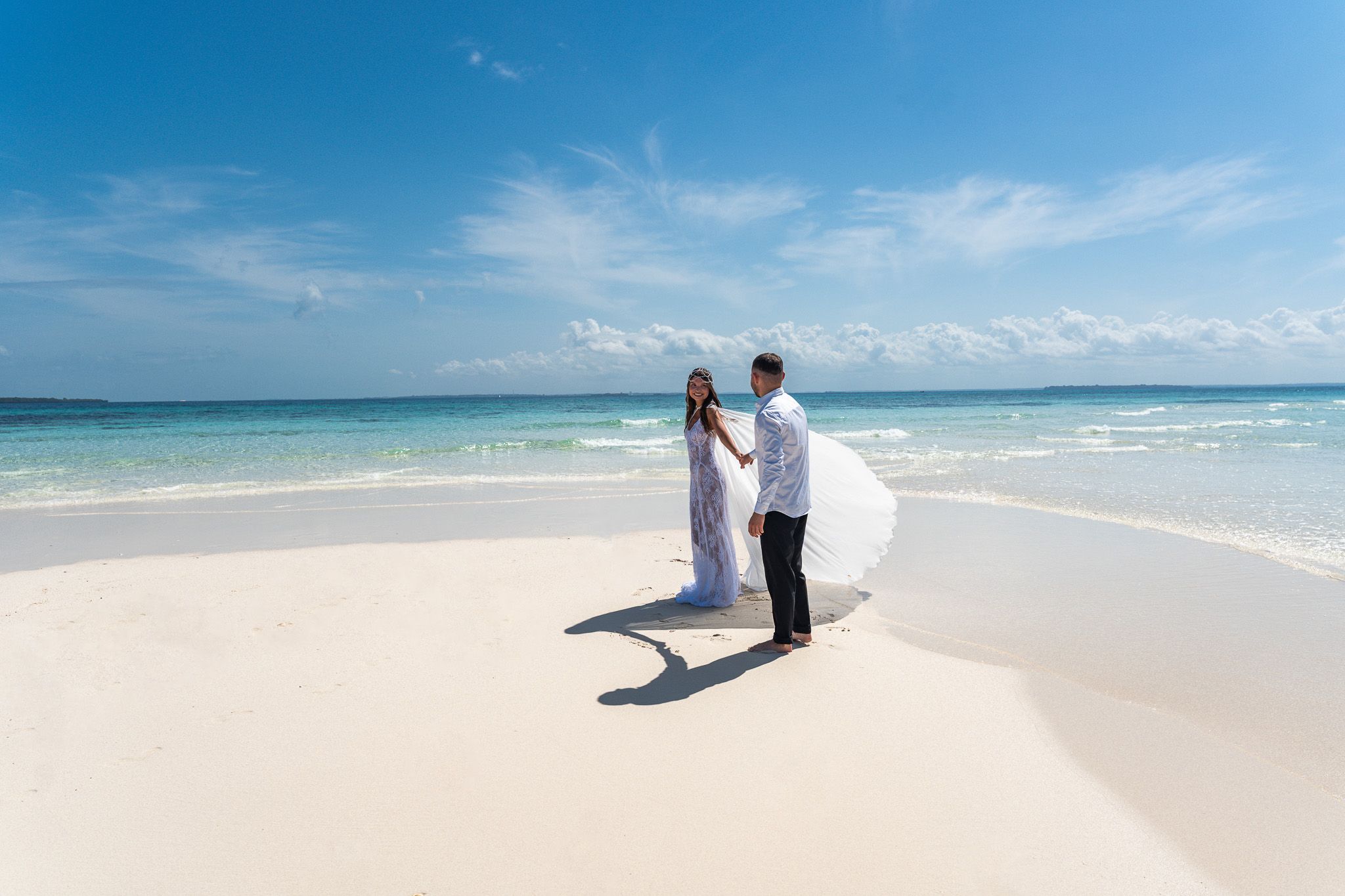 Couple holding hands walking on white sandbank beach in Zanzibar