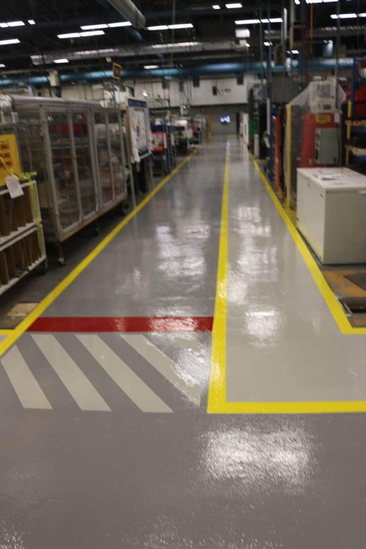 Factory floor with shiny epoxy coating, yellow and red demarcation lines and industrial racks with machinery
