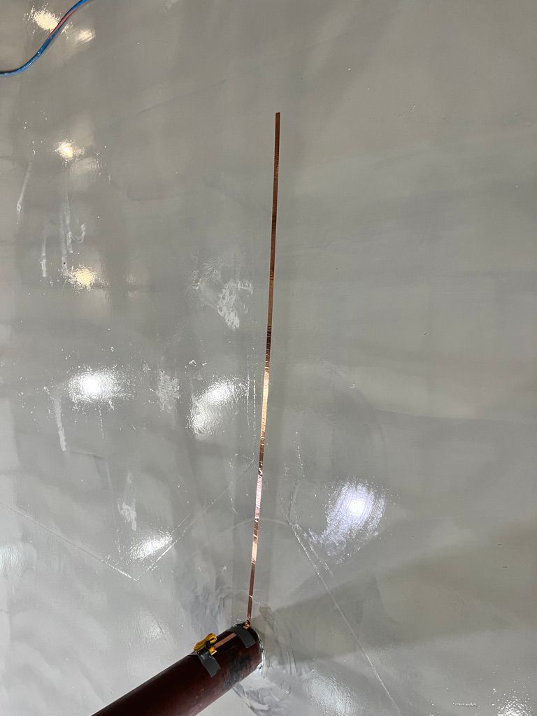 Brown cylindrical pipe with vertical copper ESD grounding strip on smooth shiny gray reflective surface