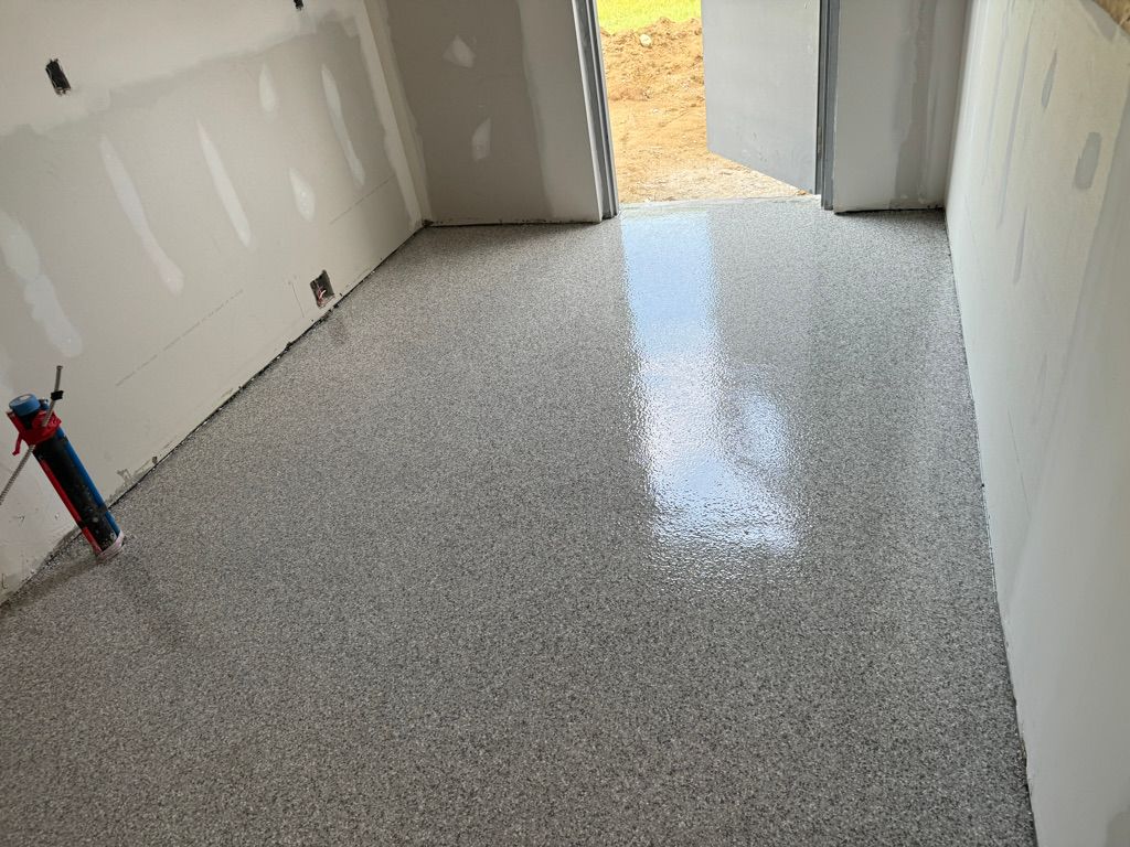 Unfinished school classroom with bare drywall and freshly installed speckled gray epoxy floor — partially open exterior door